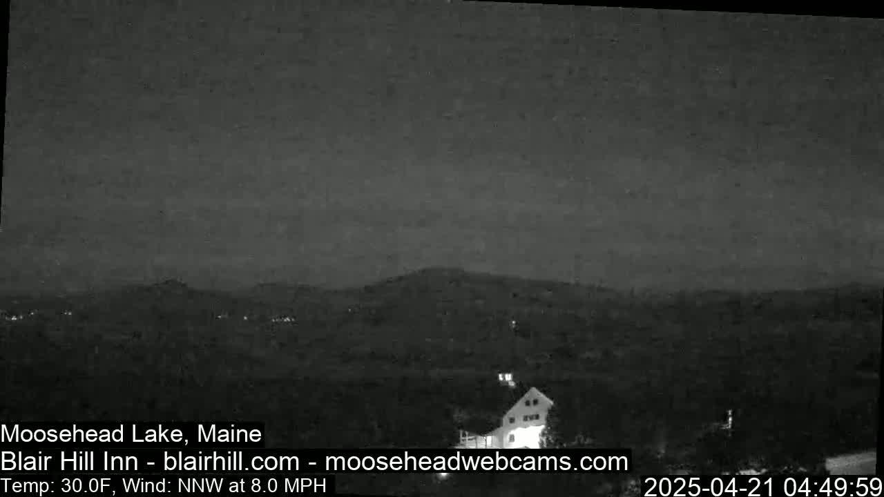 A nighttime view of a dark landscape with a building and distant hills under a mostly clear sky, with a northwest wind at 8.0 mph and a temperature of 30 degrees Fahrenheit.