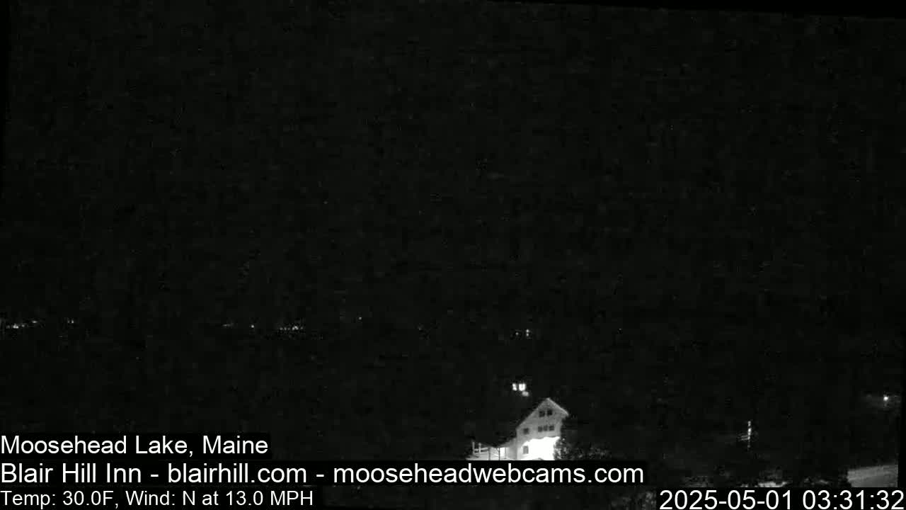 A dark, nighttime scene shows a building and a few lights in the distance under a clear, dark sky with a north wind at 13 mph and a temperature of 30°F.
