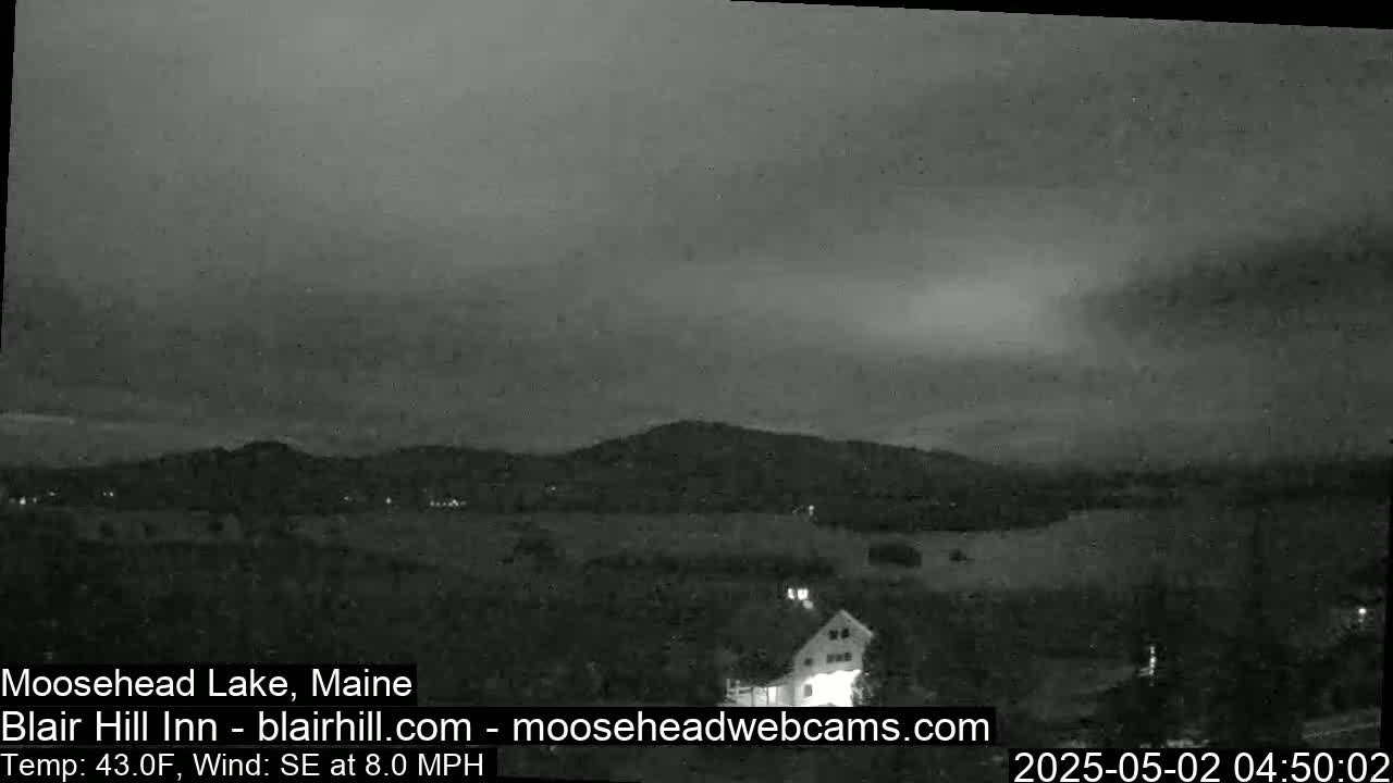 A nighttime, overcast view of a rural landscape with a farmhouse and distant hills under a southeast wind.