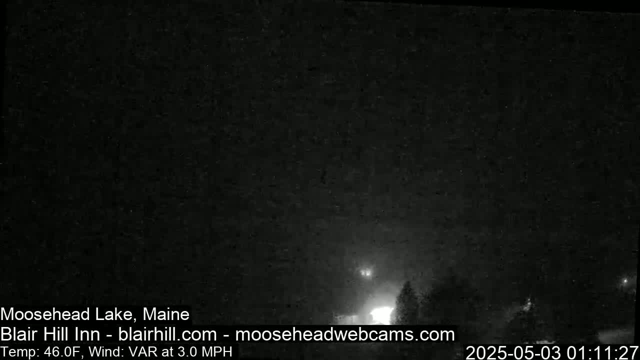A nighttime, low-light view of a dark landscape with some distant lights and a variable wind at 3.0 mph and a temperature of 46°F.