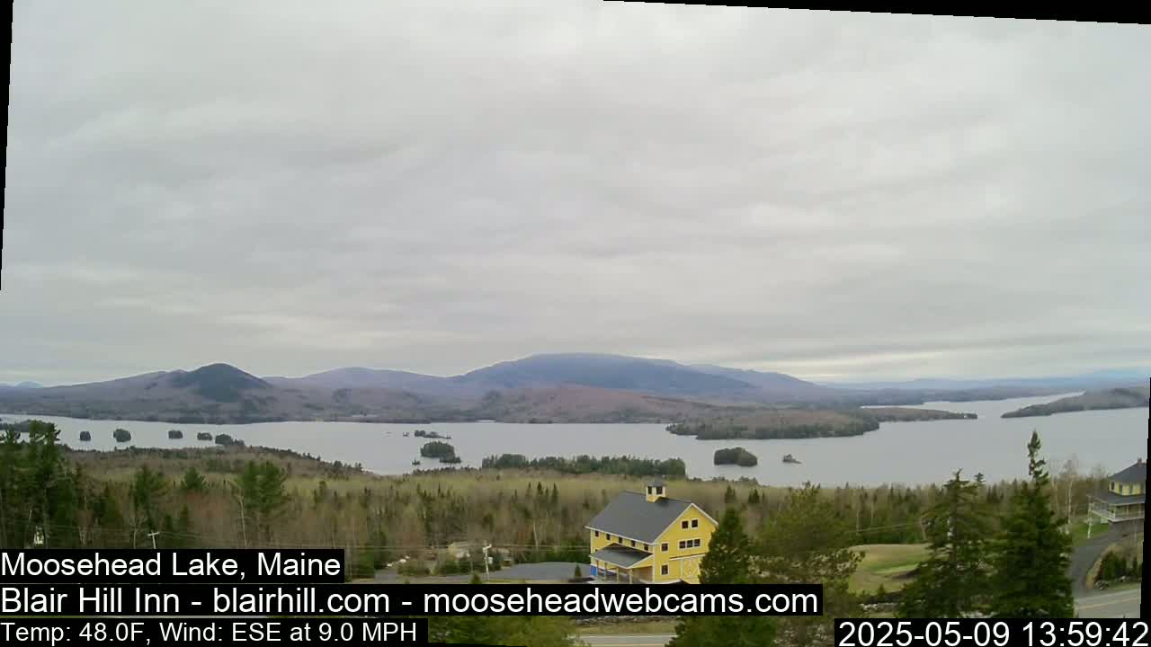 A large lake surrounded by trees and mountains is viewed from a high vantage point on an overcast day with a light wind.