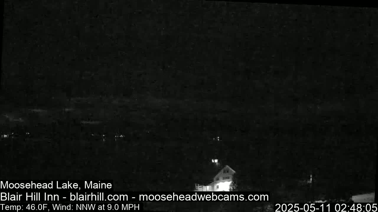 A nighttime, low-light view of a lake and a building with a dark, cloudy sky, and a 9 mph north-northwest wind.