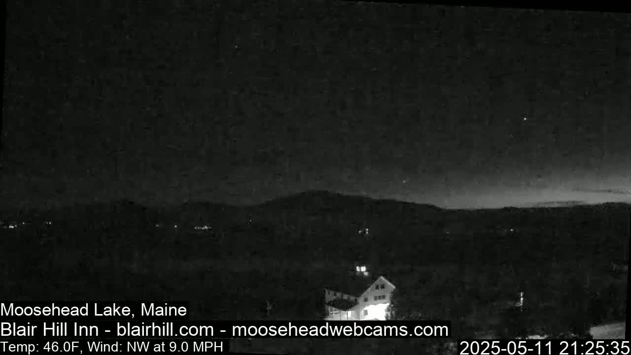 A nighttime view of a dimly lit landscape, showing a building and distant hills under a dark sky with a northwest wind at 9 mph and a temperature of 46°F.