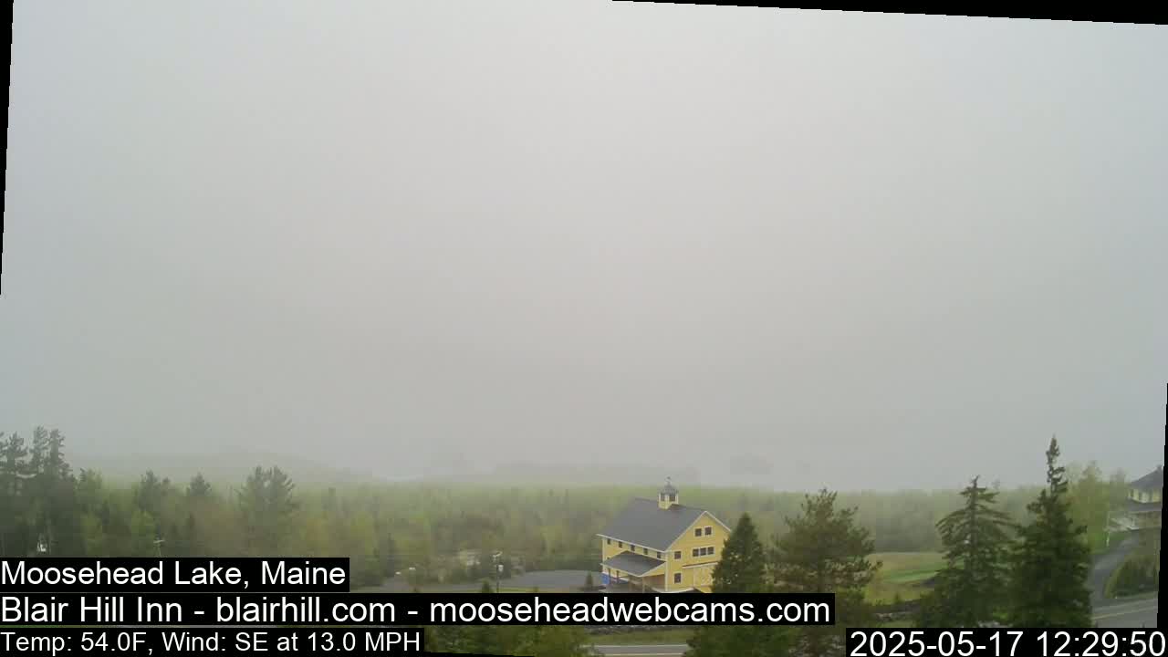 A yellow building sits among green trees in a foggy landscape, with a southeastern wind blowing at 13 mph.