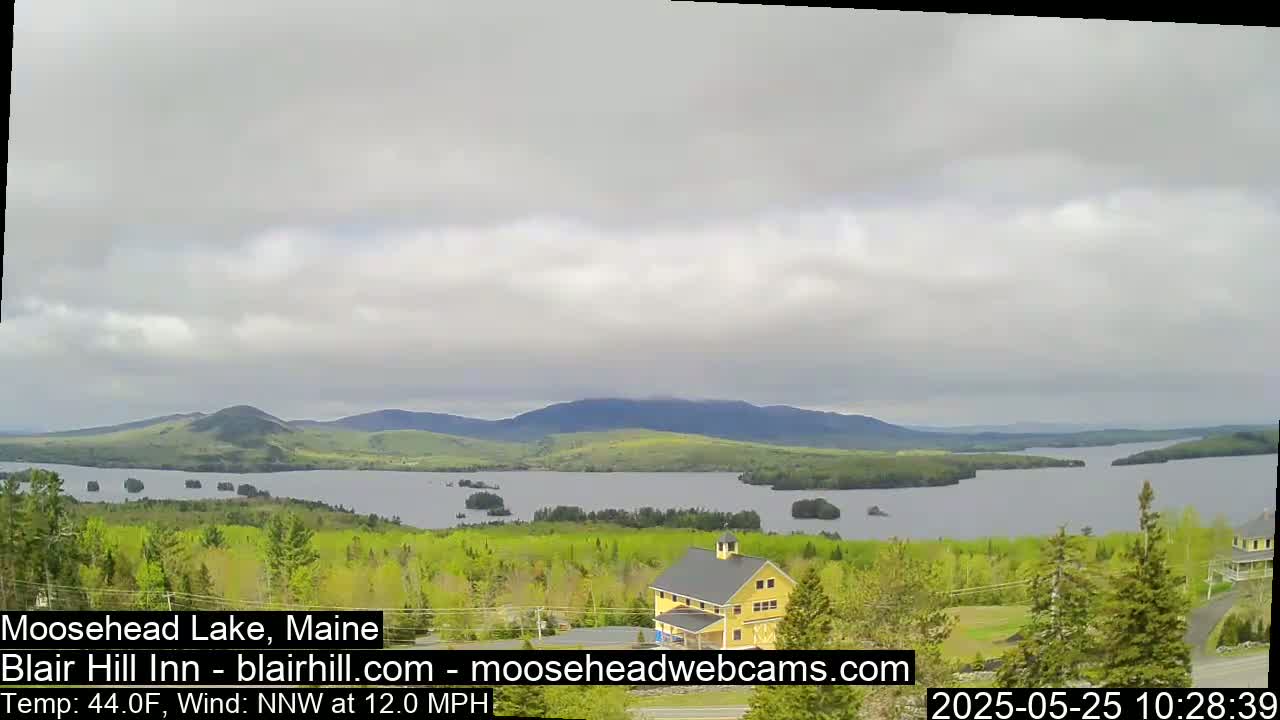 A yellow building sits on a hill overlooking a large lake with many small islands under an overcast sky, with a 12 mph wind blowing from the north-northwest.