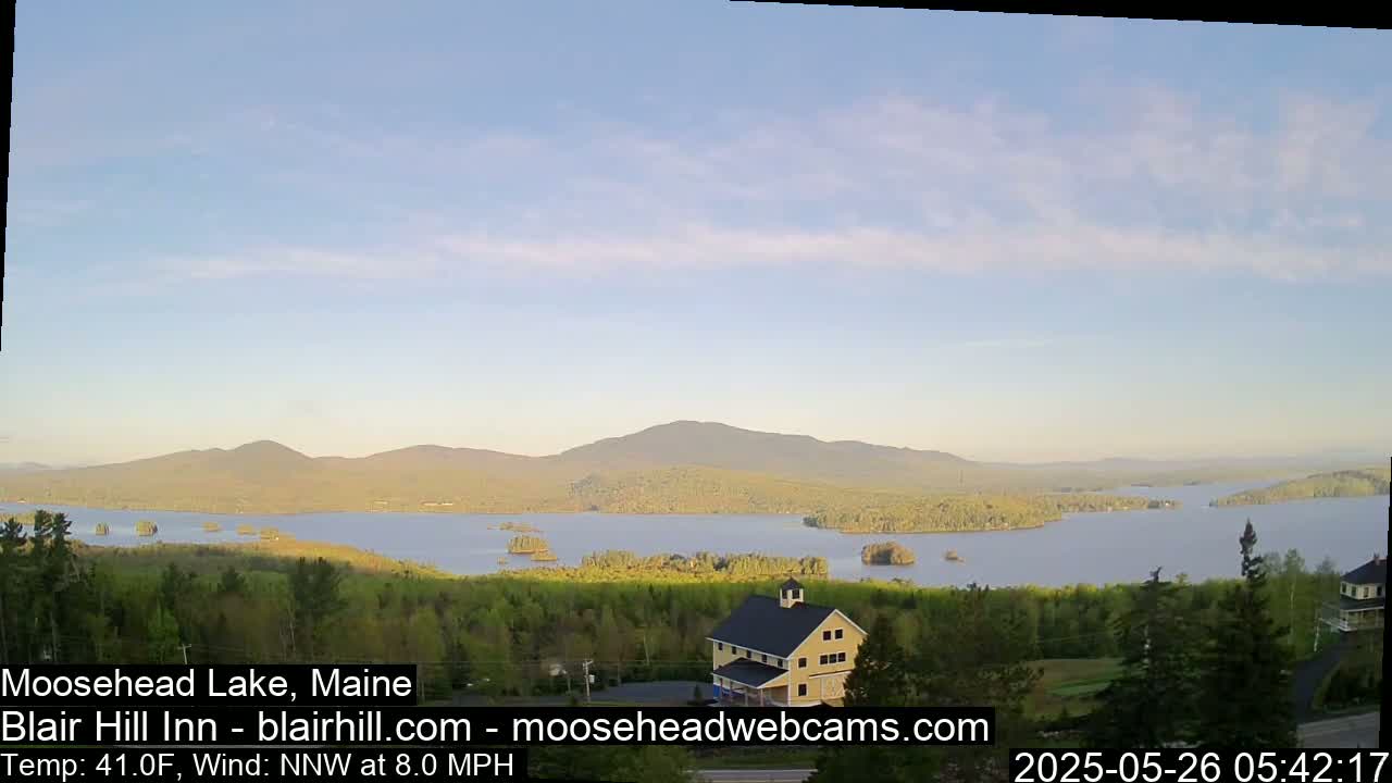 A large lake with islands and mountains in the background under a mostly clear sky is seen from an elevated vantage point, overlooking a building.