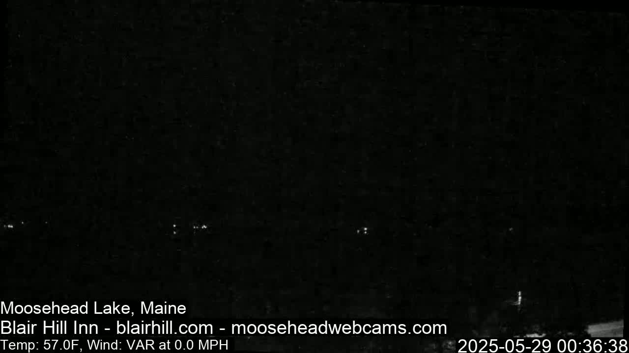 A nighttime view of a dark body of water with a few distant lights visible, under calm, clear conditions and a temperature of 57°F.