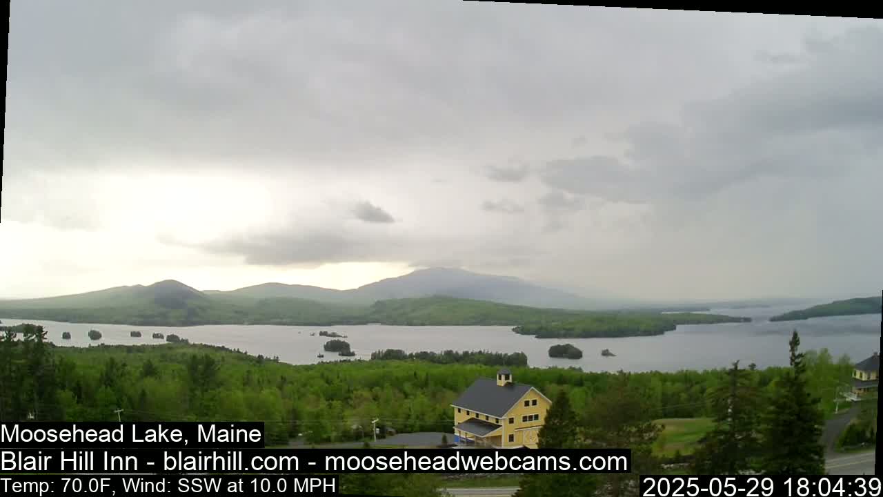 A large lake surrounded by green trees and mountains under an overcast sky.