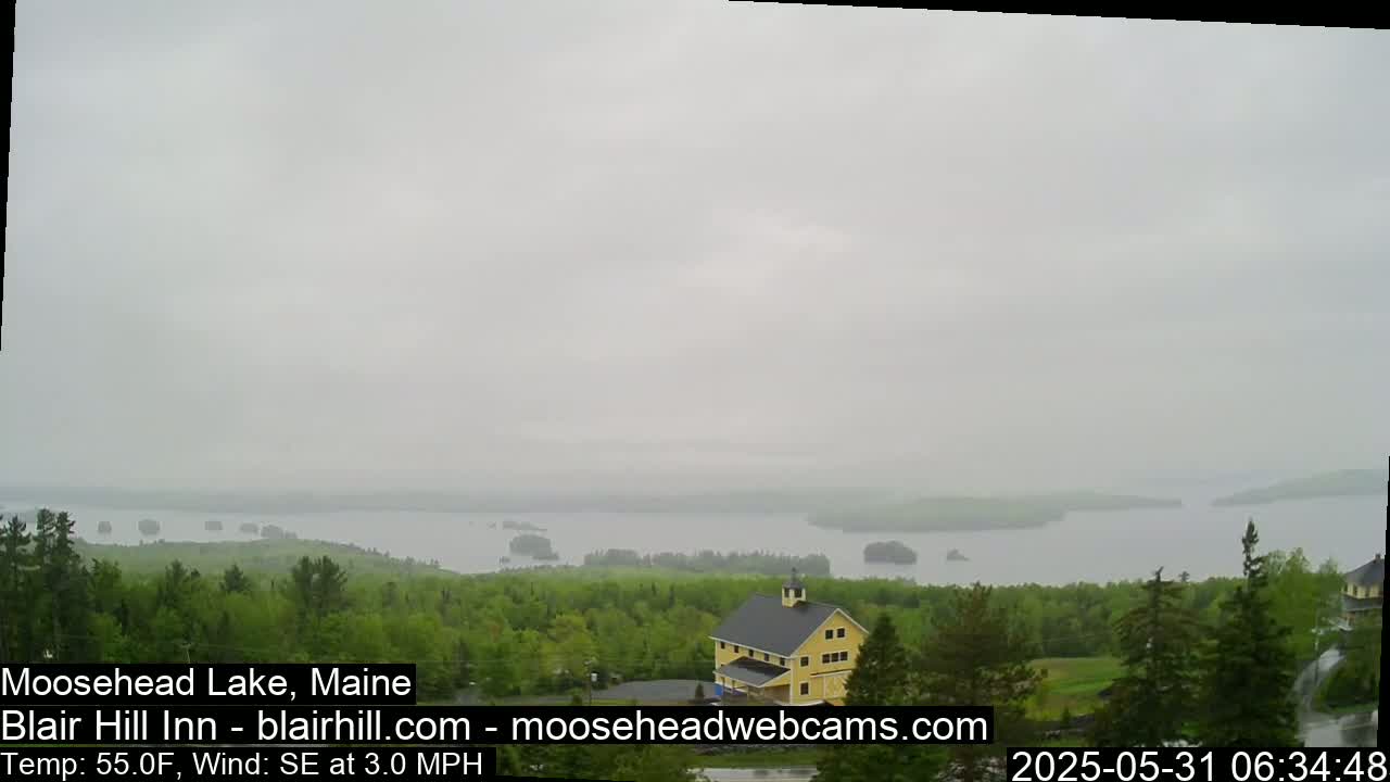 A yellow building sits on a hill overlooking a large lake under an overcast sky.