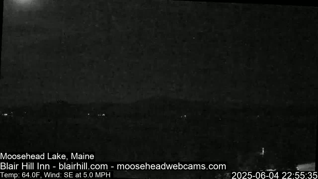 A nighttime, low-light view of a dark landscape with a few distant lights and a southeast wind at 5 mph, under a mostly clear sky.