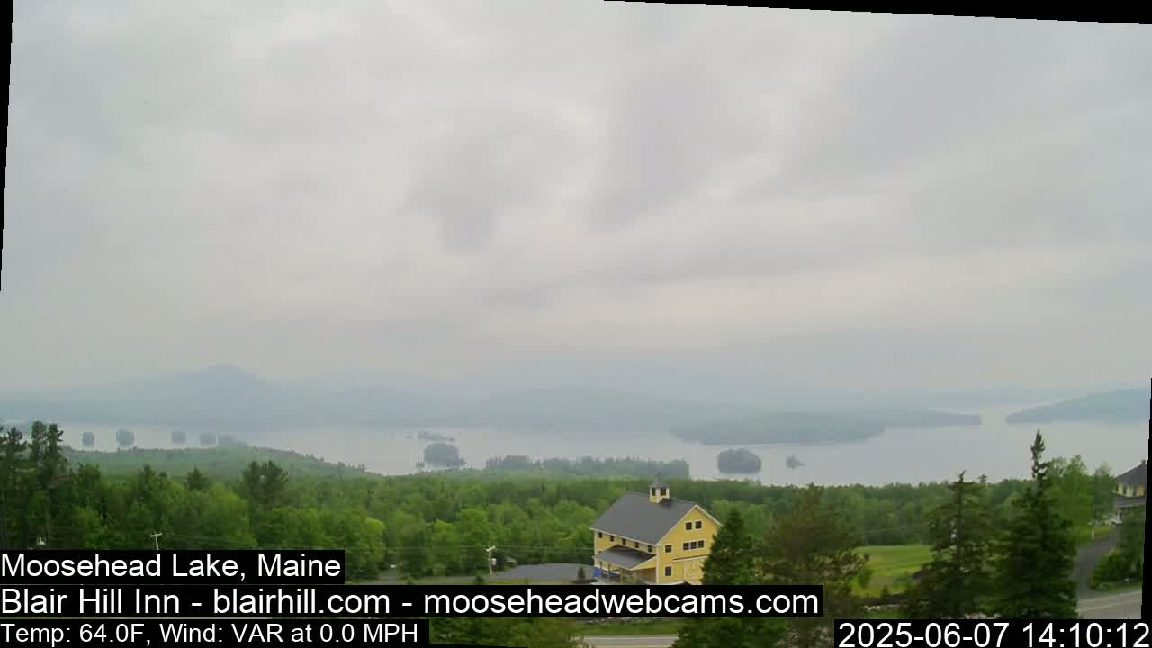 A hazy view of a lake with many islands, seen from a verdant hilltop where a yellow building stands.