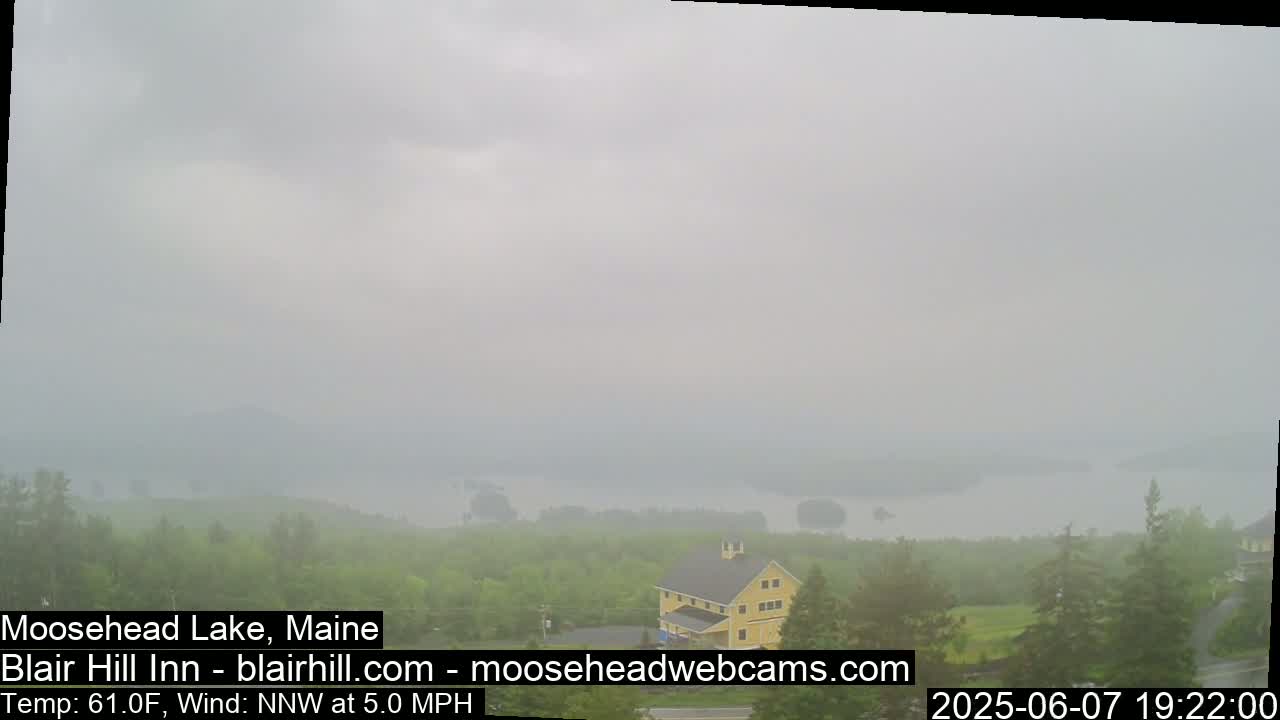 A hazy view of a lake and wooded landscape, with a yellow building visible in the foreground, under overcast skies.