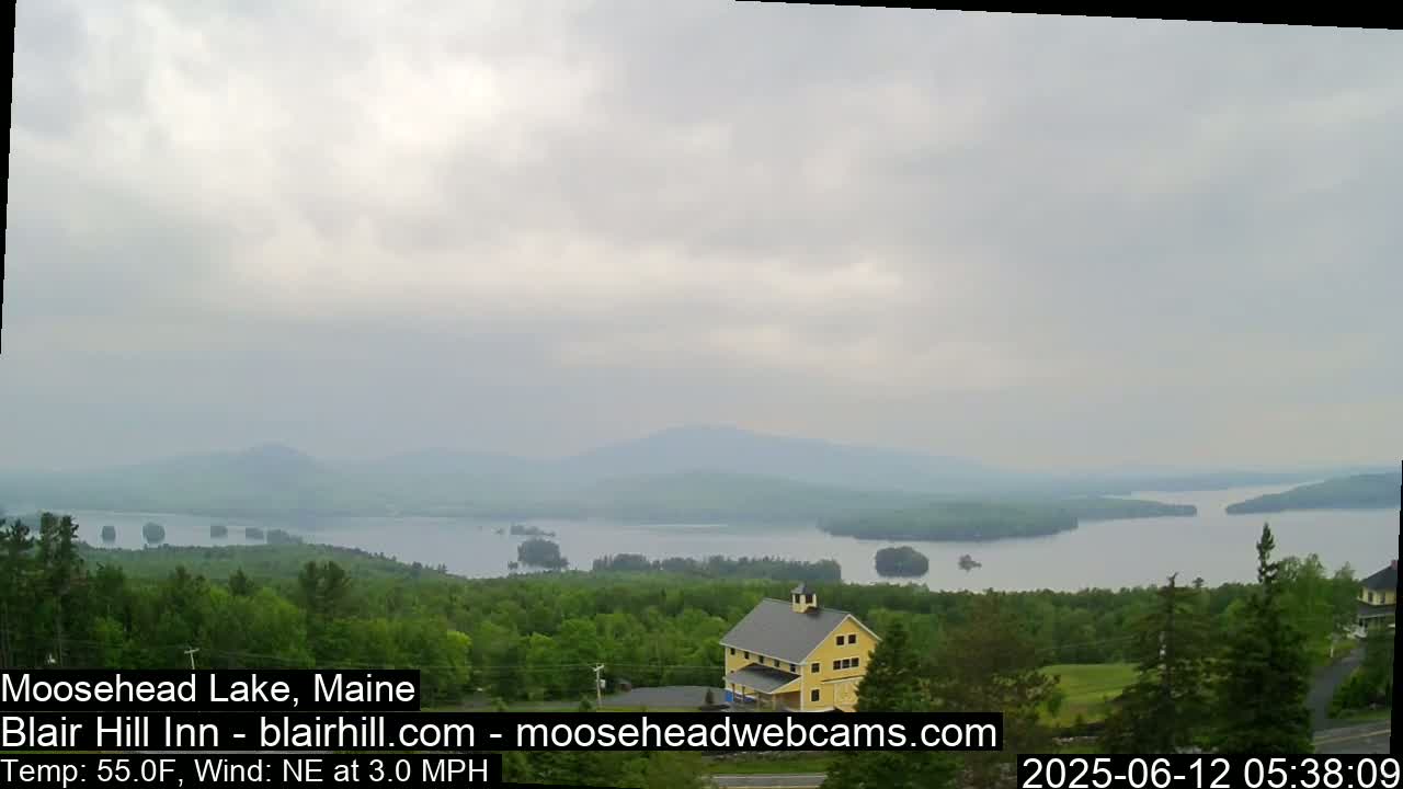 A yellow building sits on a hill overlooking a large lake with many small islands under an overcast sky.