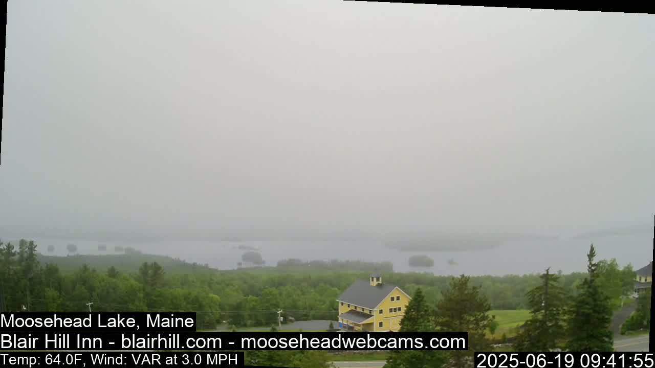 A hazy view of a lake and distant islands, with a yellow building in the foreground and green trees.