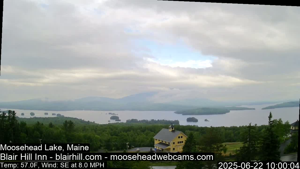 A yellow building sits on a hill overlooking a large lake dotted with islands under a cloudy sky.