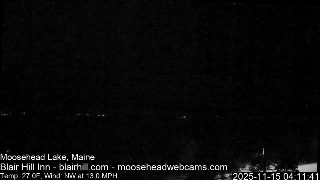 The image shows an extremely dark outdoor scene at night, with only a few faint, distant lights visible along a low horizon under what appears to be a clear sky.