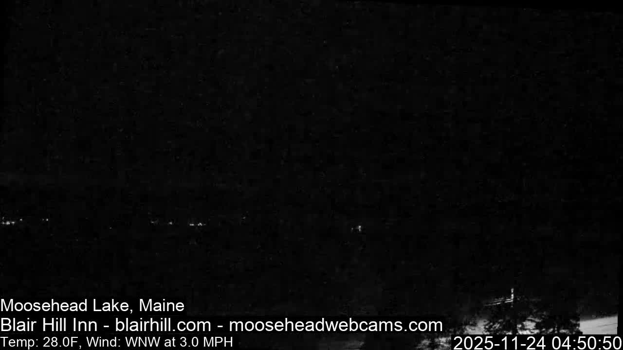 A very dark image depicts a clear night over a distant landscape, with scattered faint lights barely visible across the horizon and a shadowy structure indistinctly outlined in the lower right.