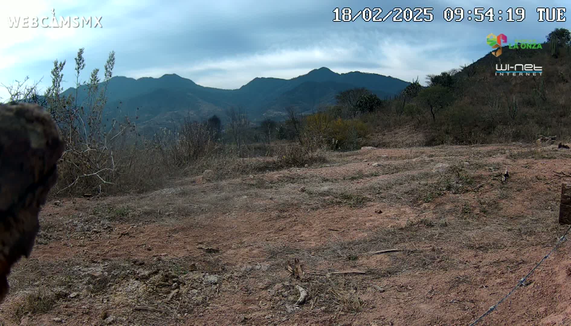 A mostly clear sky overlooks a dry, brown, sparsely vegetated landscape with mountains in the background.