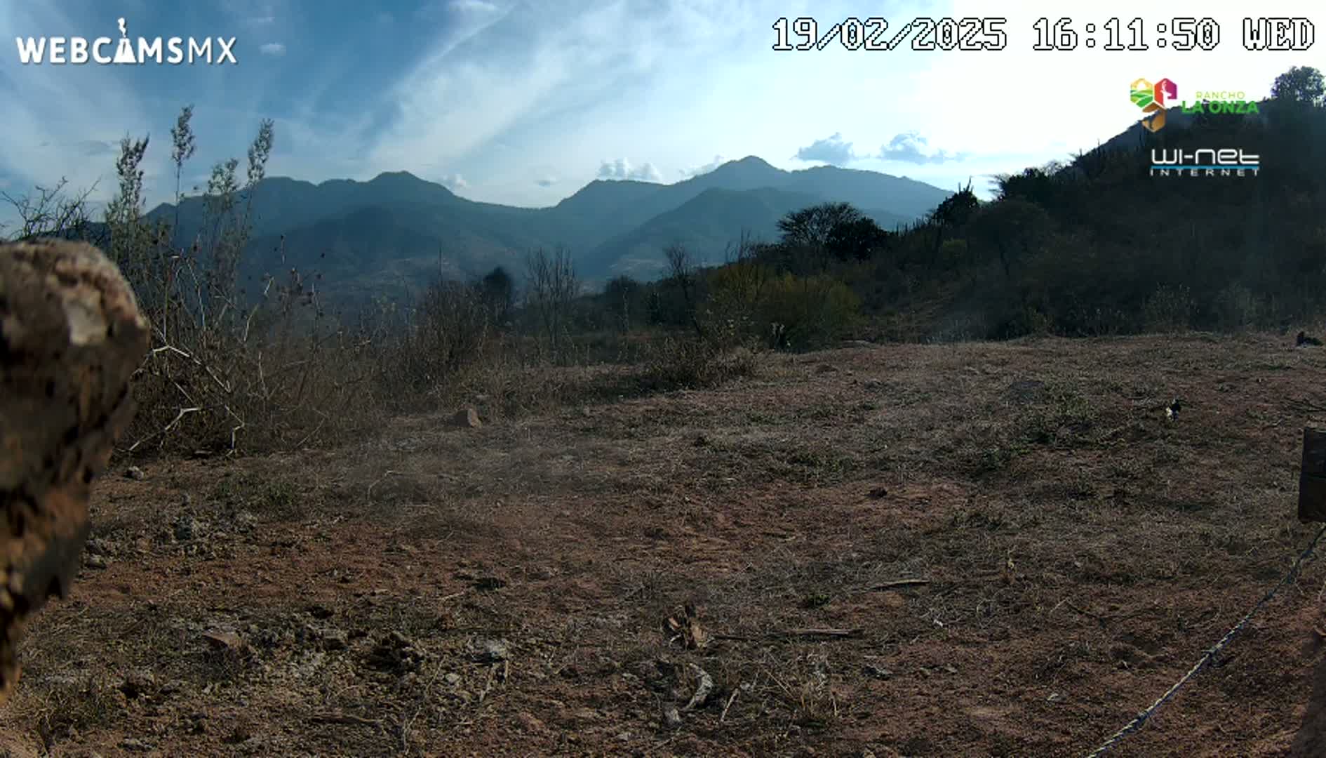 A mostly clear, daytime view of a dry, brown landscape with sparse vegetation and distant mountains under a partly cloudy sky.