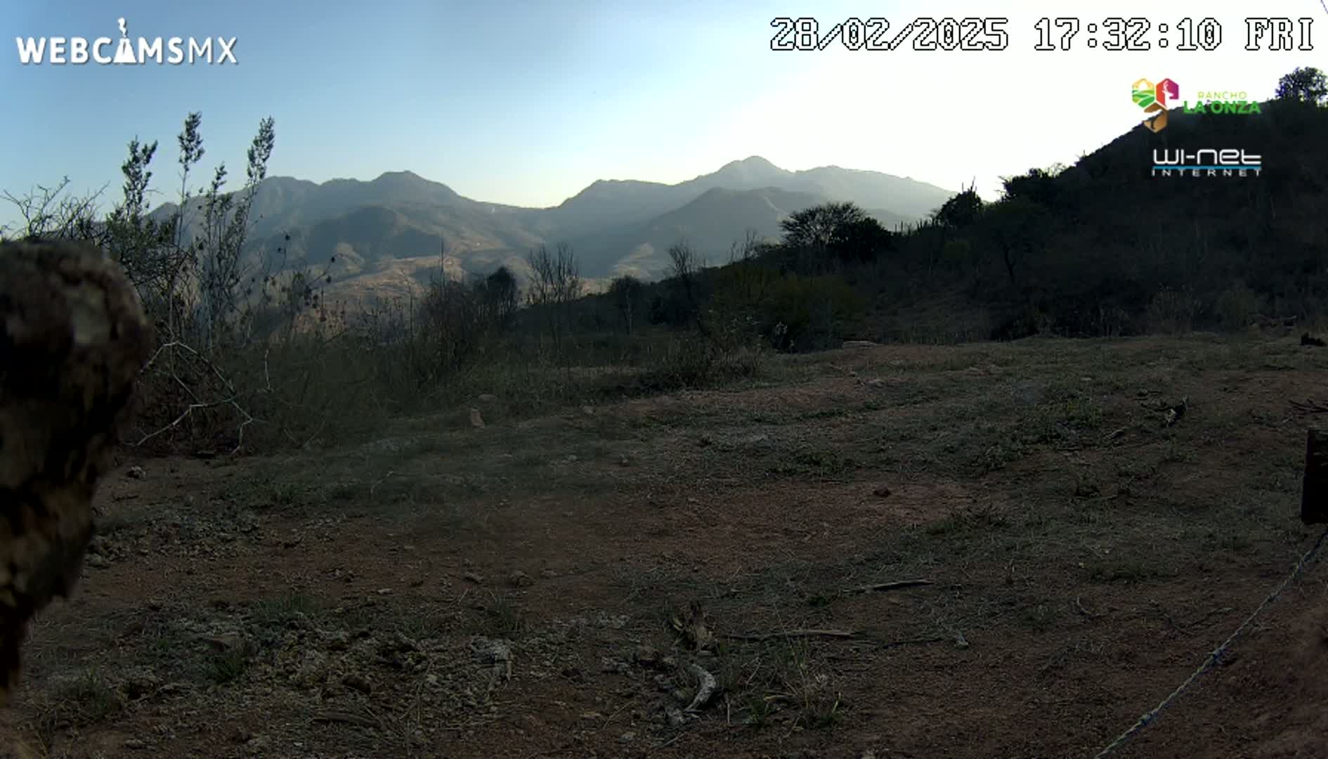 A dirt path overlooks a scrubby landscape and distant mountains under a clear, twilight sky.