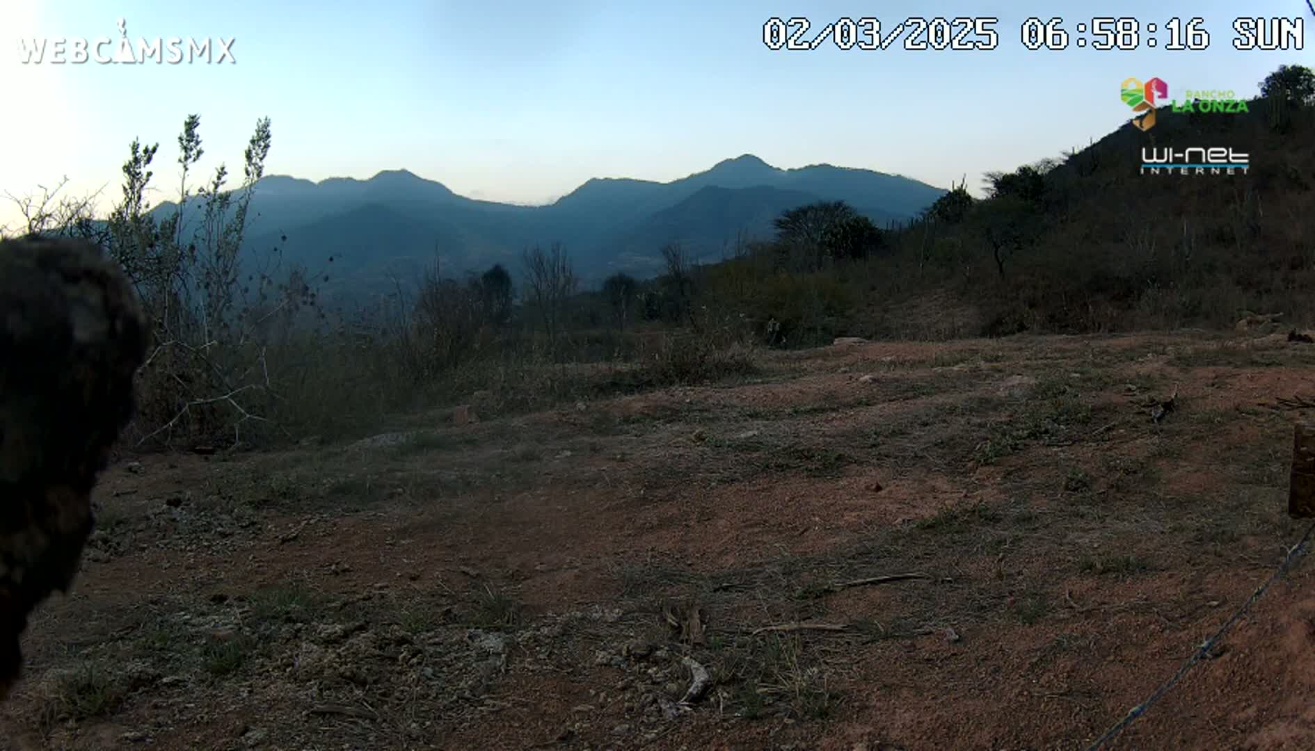 A dusty, barren landscape with sparse brush and distant, dark mountains under a twilight sky.