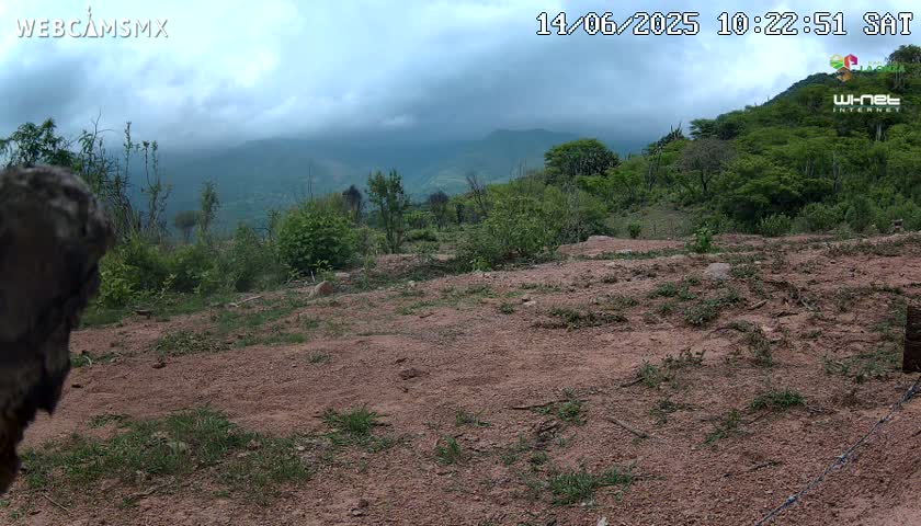 A mostly cloudy day reveals a dirt path overlooking a hilly landscape covered in green vegetation under an overcast sky.