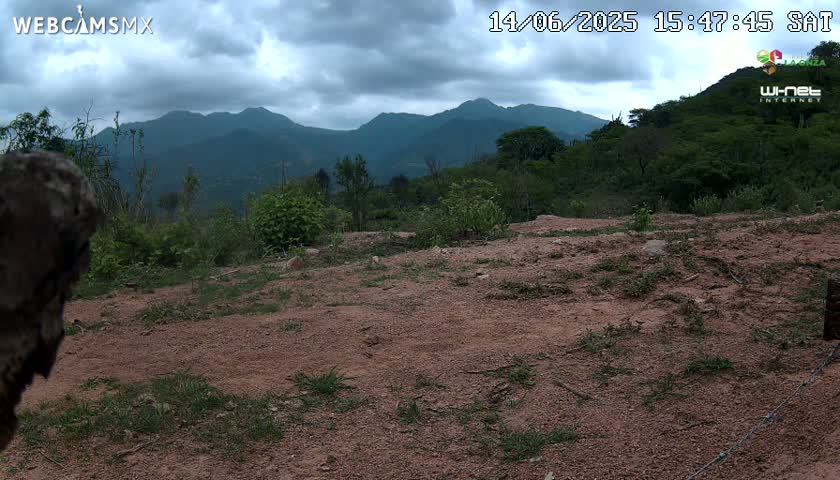 A mostly cloudy day reveals a dirt path overlooking a hilly landscape covered in green vegetation under an overcast sky.