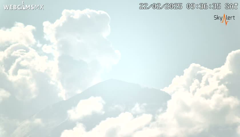 A mountain peak is partially visible beneath a bright, partly cloudy sky.