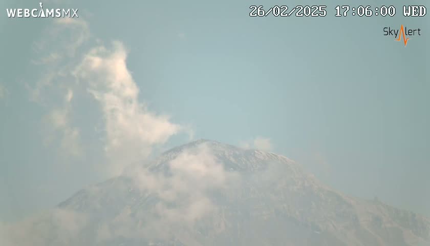 A snow-capped mountain is partially obscured by clouds under a hazy sky.