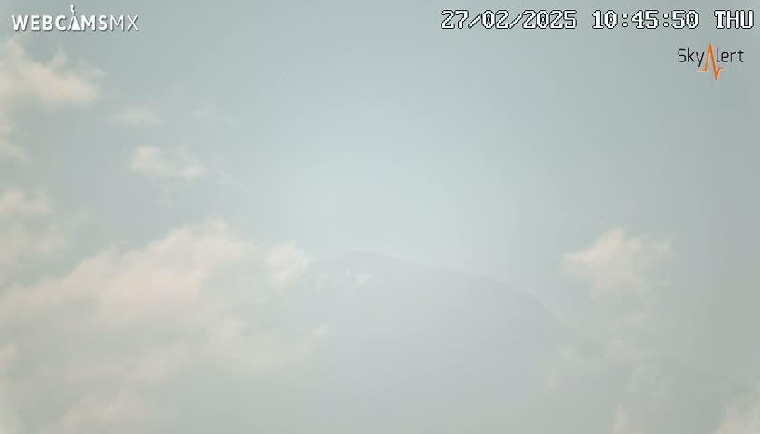 A mostly clear sky with scattered, thin clouds is visible, with a hazy mountain range faintly seen in the distance.