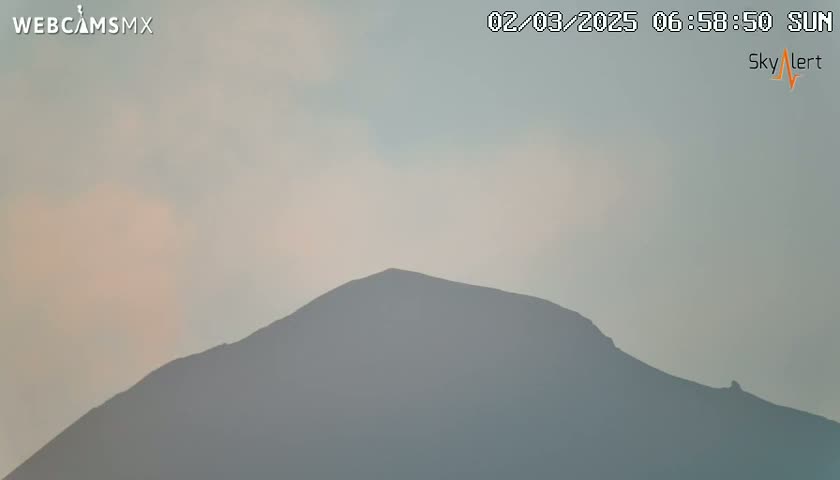 A hazy, light-grey sky hangs over a dark-grey, silhouetted mountain.