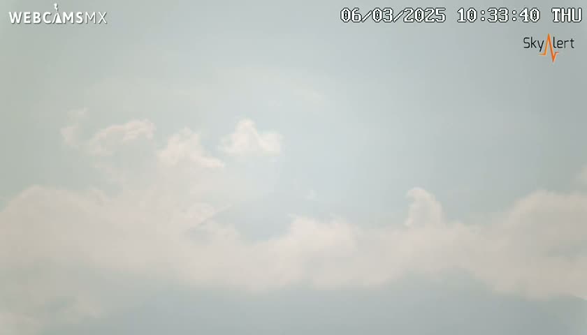 A mostly sunny sky with scattered cumulus clouds is visible.