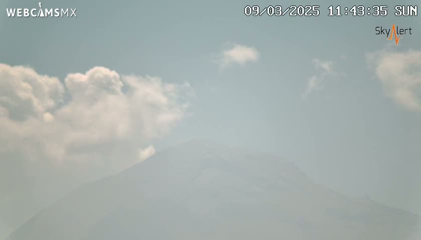A hazy mountain is visible under a partly cloudy, sunny sky.
