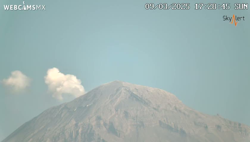 A large, gray mountain is partially obscured by a small, white cloud plume under a clear, light-blue sky.