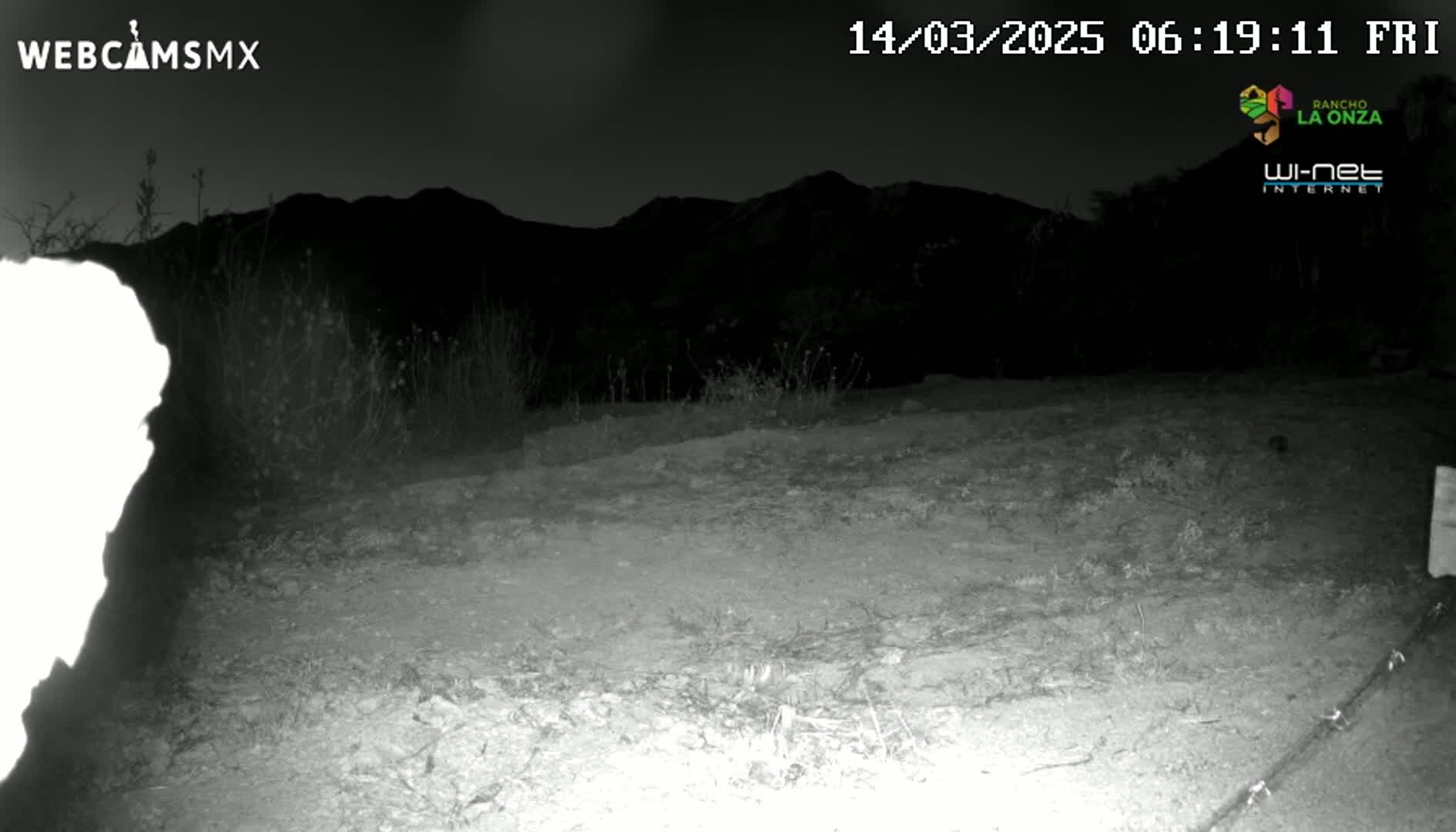A nighttime, low-light image shows a dirt area in front of dark mountains under a clear, dark sky.