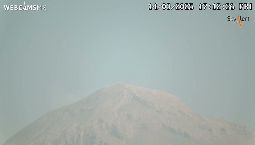 A hazy view of a large, light brown mountain is seen under a light-grey sky.