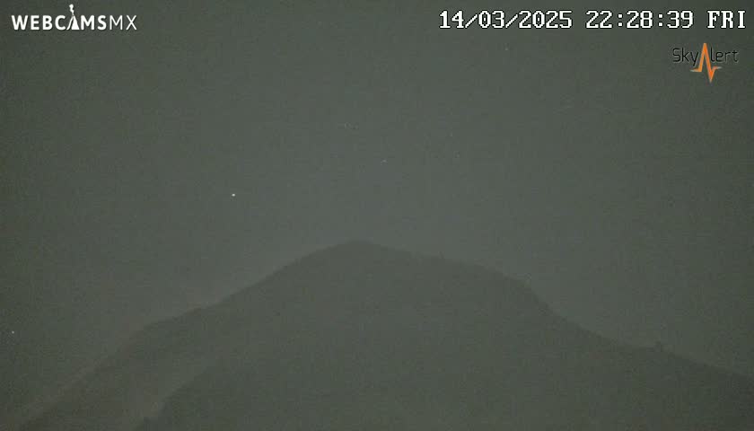 A dark, hazy night scene shows a silhouetted mountain under a mostly clear sky with a few faint stars visible.