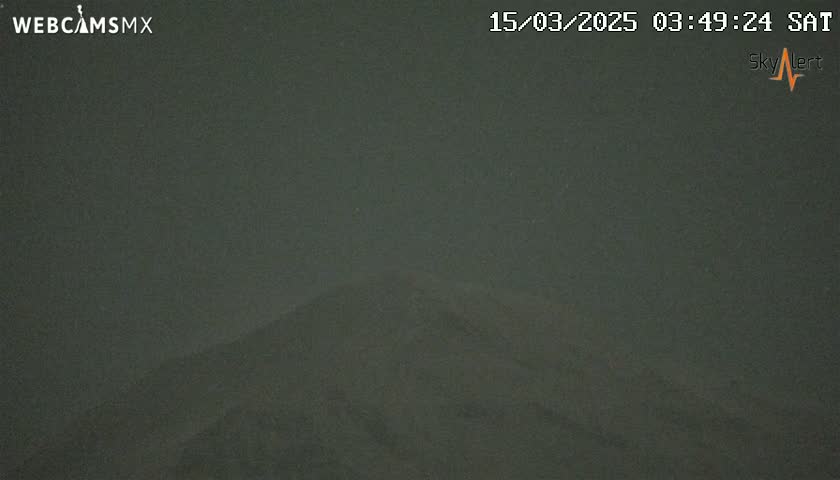 A dark, nighttime image shows a mountain silhouetted against a hazy, dark sky.
