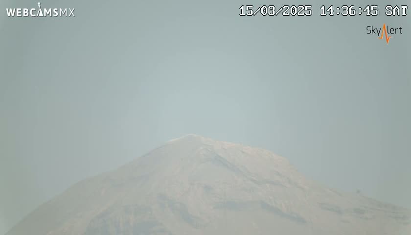 A hazy view shows a large, light-brown mountain under a light-grey sky.