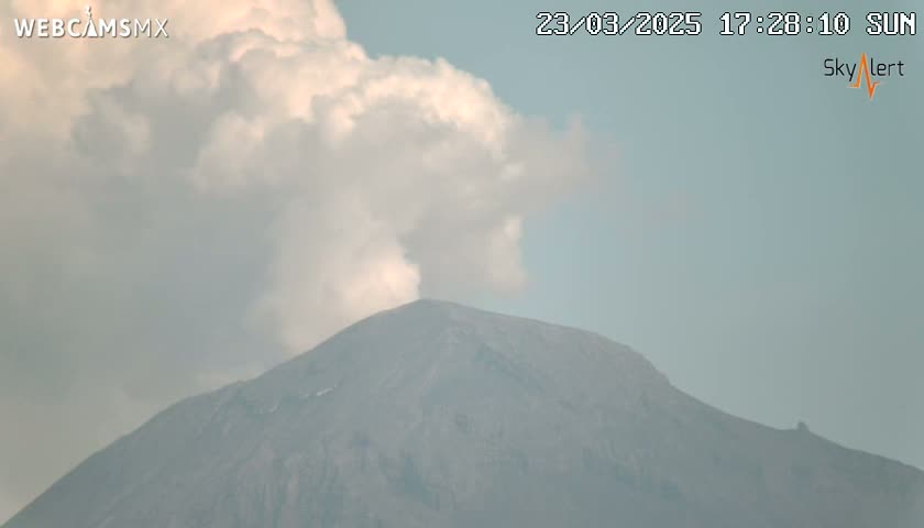A large, dark-gray mountain is partially obscured by a plume of light-gray smoke or steam under a mostly cloudy sky.