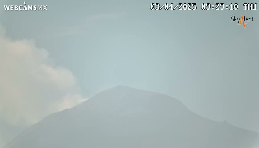 A hazy, light-grey sky obscures a distant mountain range under diffuse cloud cover.