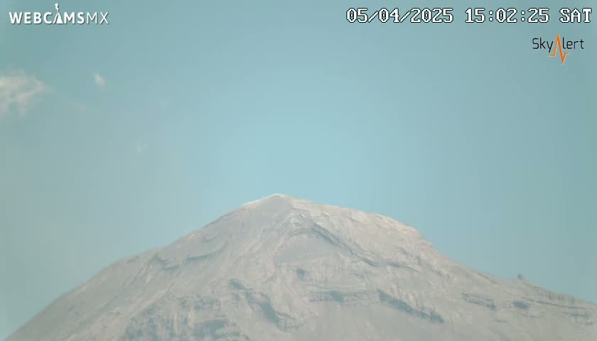 A mostly clear sky is visible above a large, gray mountain.