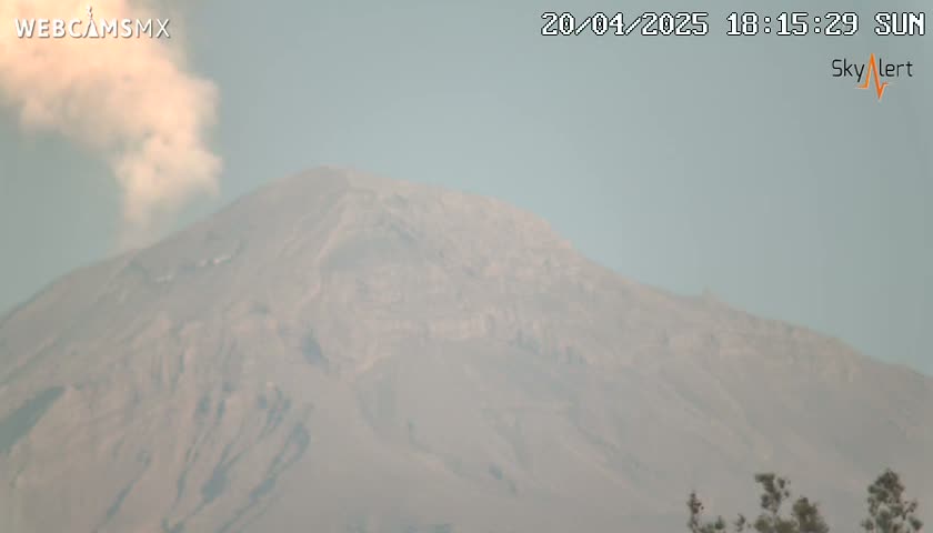 A hazy plume of smoke rises from a large, light-grey mountain on a hazy day.