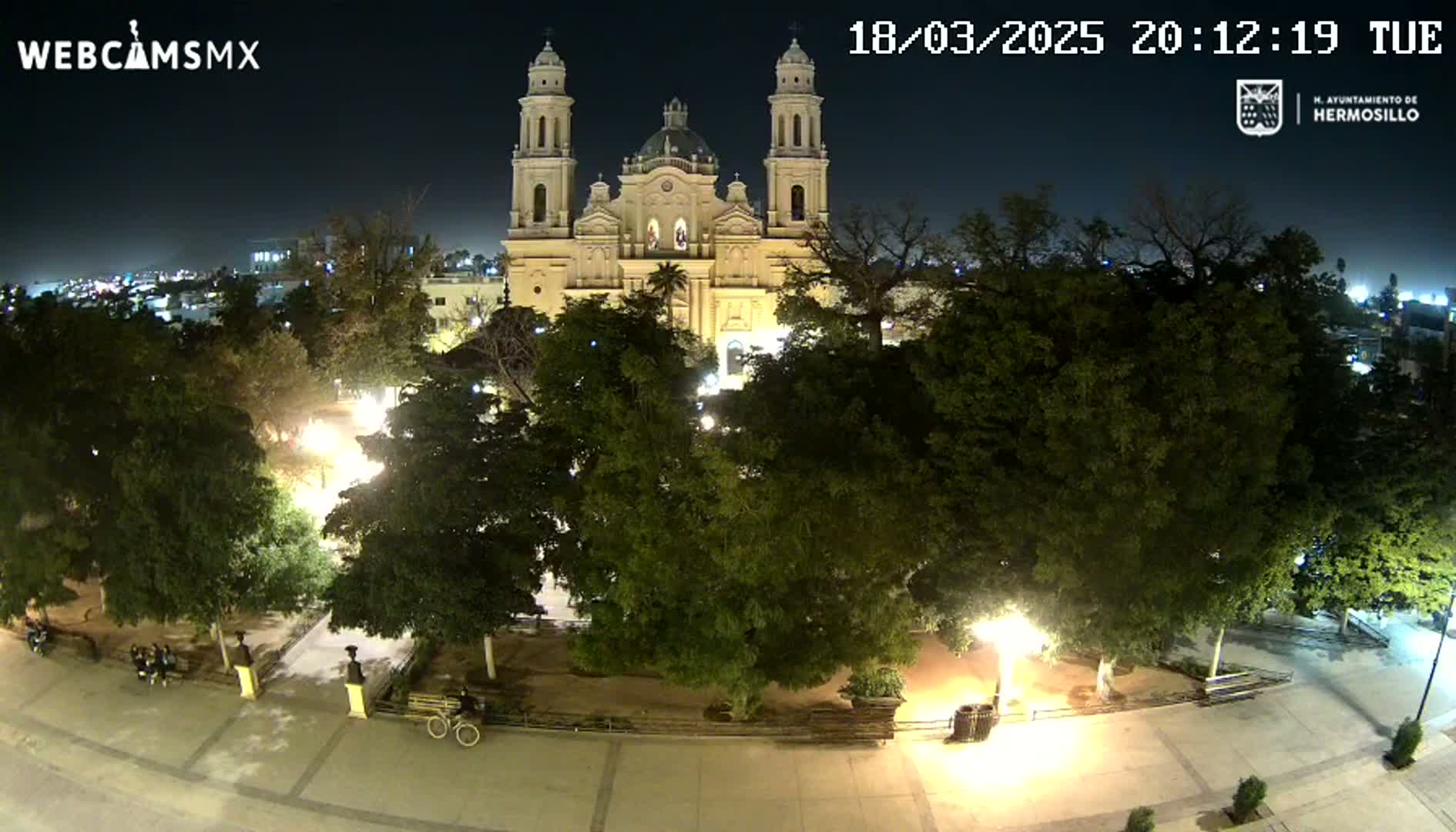 A nighttime view of a plaza with a large cathedral in the background, under a clear sky.