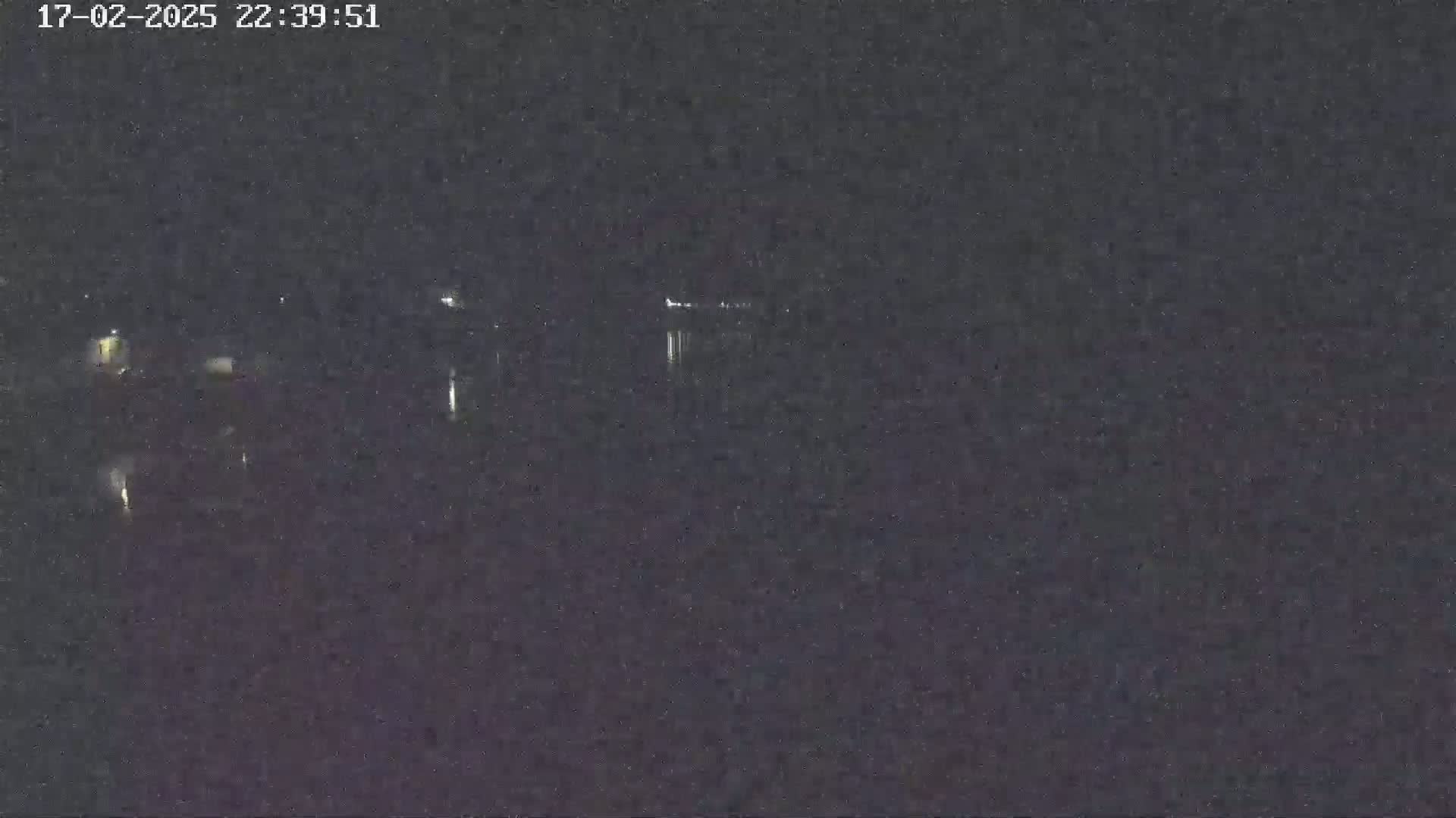 A nighttime, low-light view of a dark body of water with faint lights visible on the far shore.