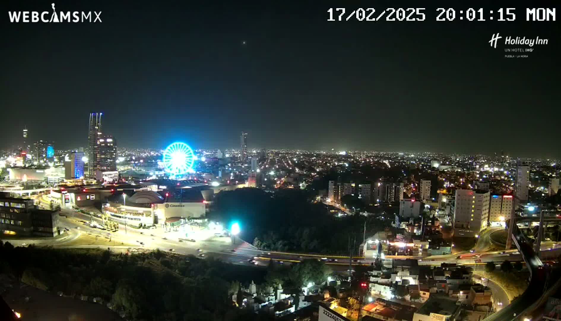 A nighttime aerial view of a city with a Ferris wheel and illuminated buildings, under a clear sky.