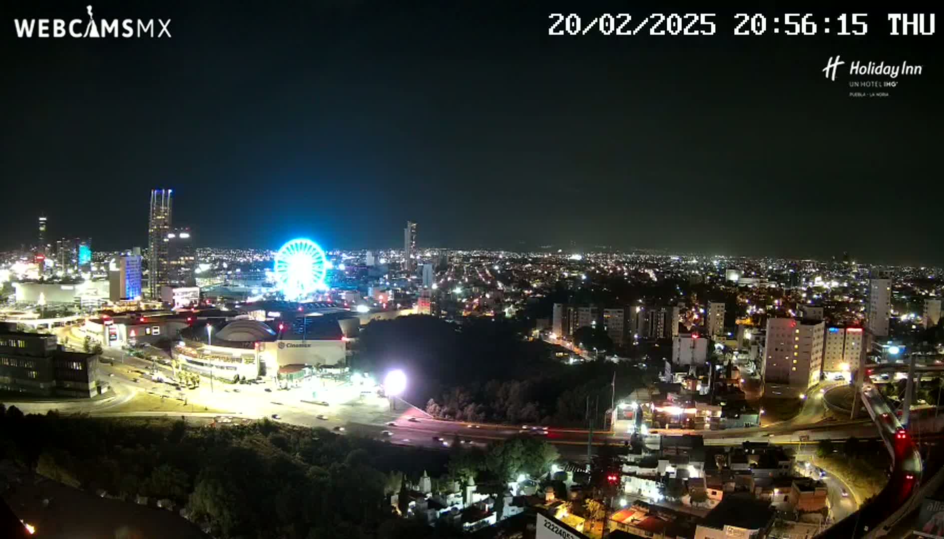 A nighttime, illuminated cityscape with a Ferris wheel and a highway visible, under clear skies.
