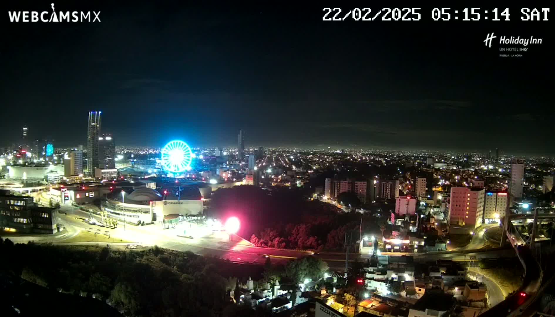 A nighttime view of a city illuminated by streetlights, featuring a Ferris wheel and several buildings, under a clear sky.