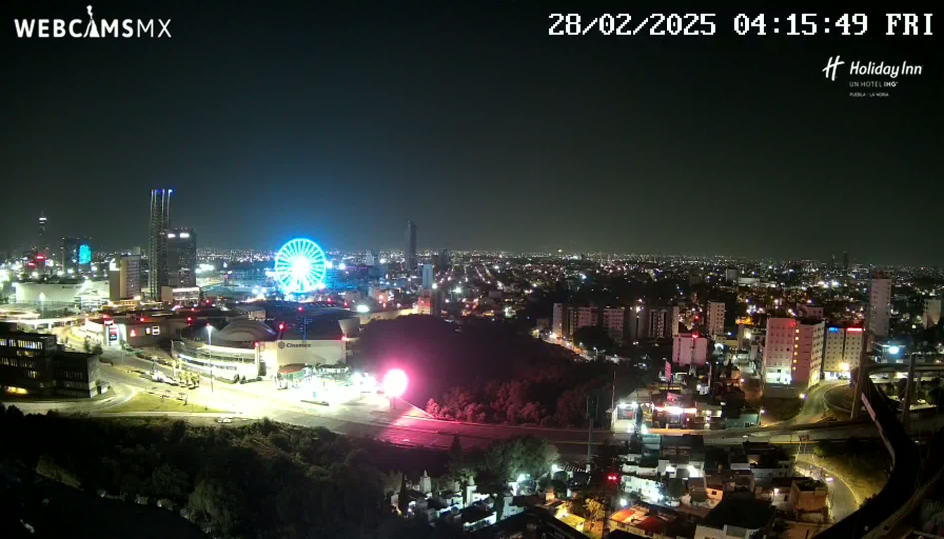 A nighttime cityscape with a Ferris wheel and illuminated buildings, under a clear sky.