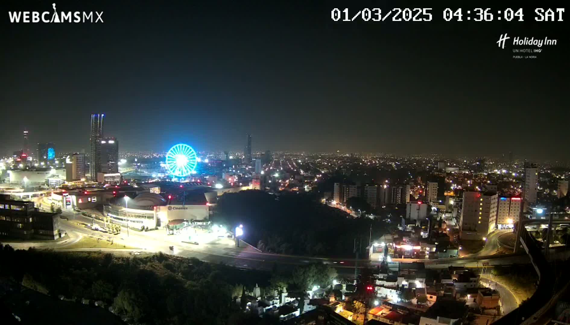 A nighttime cityscape with a Ferris wheel and numerous illuminated buildings, under a hazy sky.